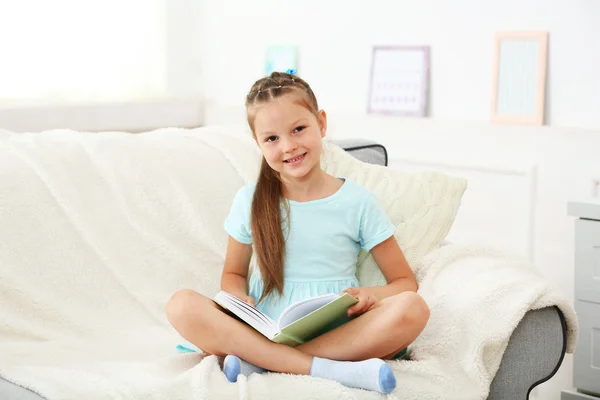 Kleines Mädchen sitzt mit Buch auf Sofa — Stockfoto