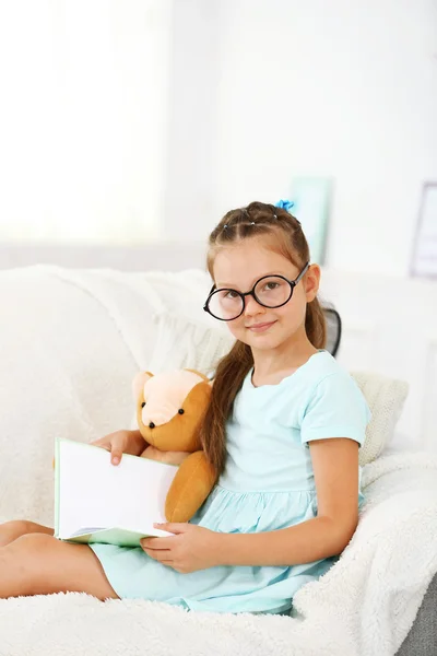 Petite fille assise sur un canapé avec un livre — Photo