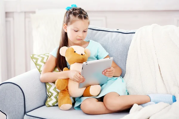Kleines Mädchen mit Teddybär und Tablet — Stockfoto