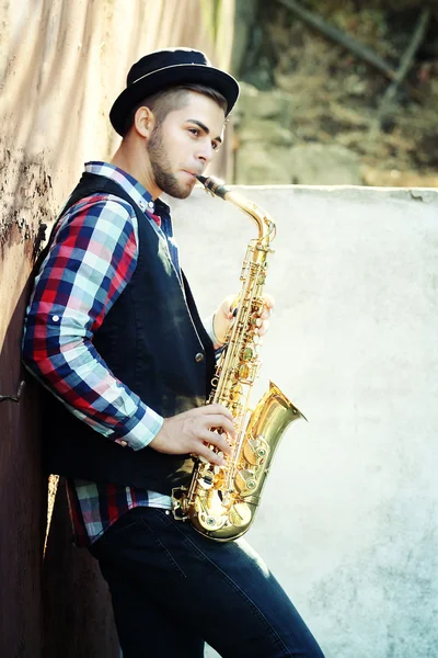 Joven tocando el saxofón afuera cerca de la vieja pared — Foto de Stock