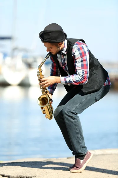 Young man playing on saxophone on the riverside — Stock Photo, Image
