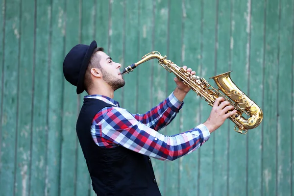 O músico toca saxofone em fundo de madeira verde — Fotografia de Stock