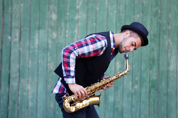 El músico toca el saxofón sobre fondo de madera verde — Foto de Stock