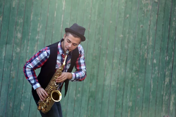 The musician plays saxophone on green wooden background — Stock Photo, Image