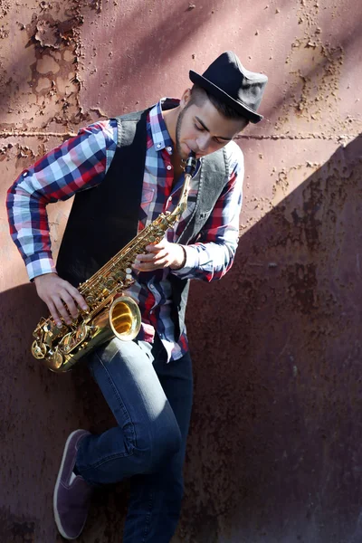 Przystojny młody mężczyzna gra saksofon na stary tło ściany brązowy — Zdjęcie stockowe