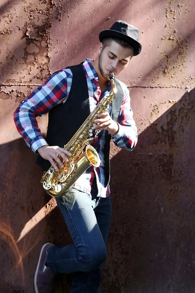 Schöner junger Mann spielt Saxophon auf altem braunen Wandhintergrund — Stockfoto