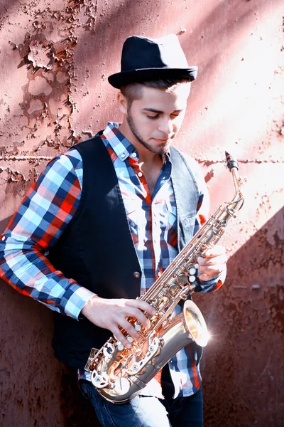 Bello giovane uomo gioca sax su vecchio marrone parete fondo — Foto Stock