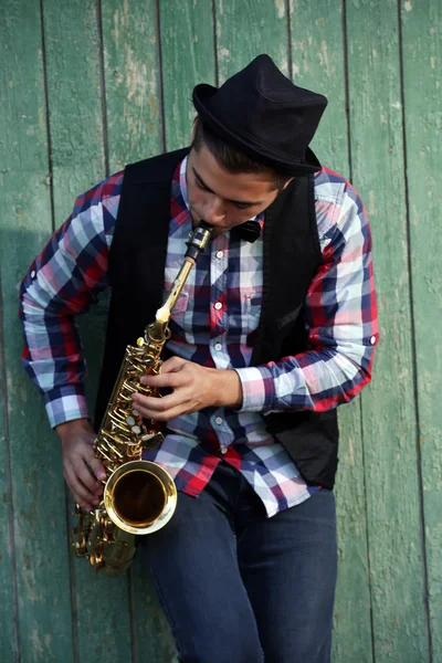 Bonito homem toca saxofone no fundo de madeira verde — Fotografia de Stock