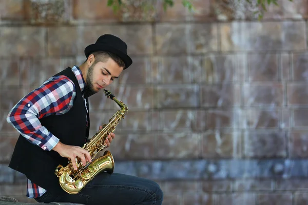 Przystojny młody mężczyzna gra saksofon na tle kamiennego muru — Zdjęcie stockowe
