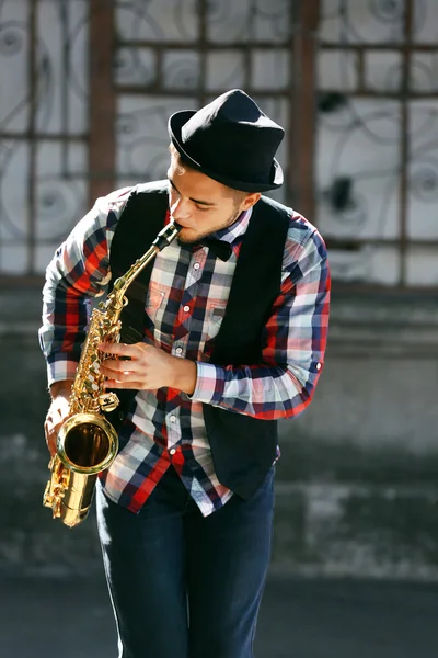 Junger Mann spielt Saxofon vor städtischem Hintergrund — Stockfoto