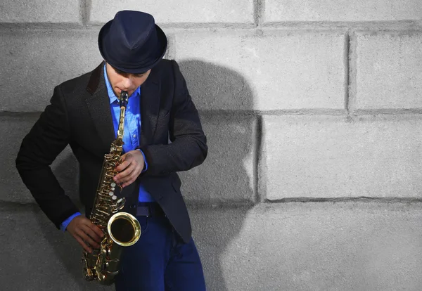 Elegante giovane uomo con sax su sfondo muro di mattoni — Foto Stock