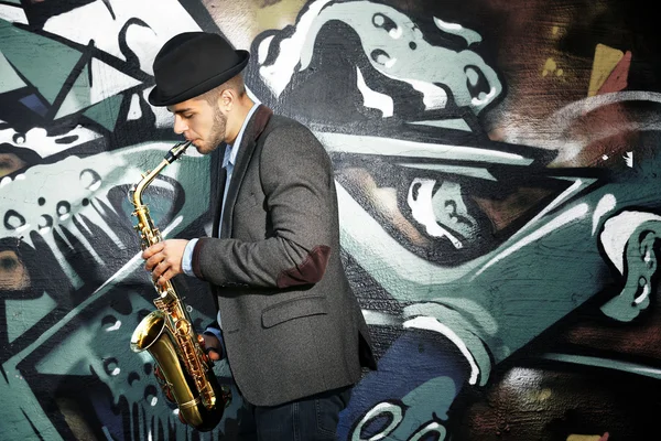 Jovem com saxofone fora perto da parede pintada velha — Fotografia de Stock