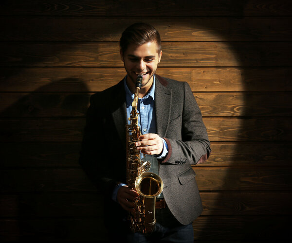 Elegant saxophonist plays jazz on wooden background