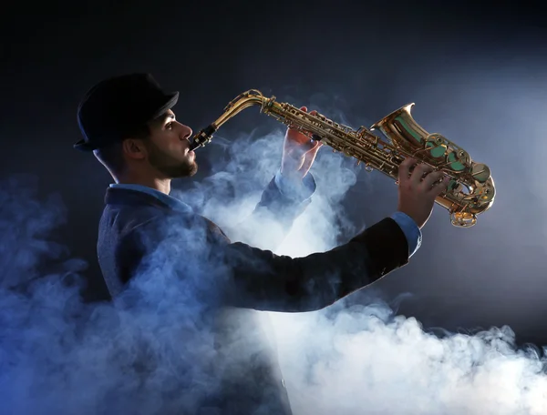 Elegante saxofonista toca jazz sobre fondo oscuro en un humo —  Fotos de Stock