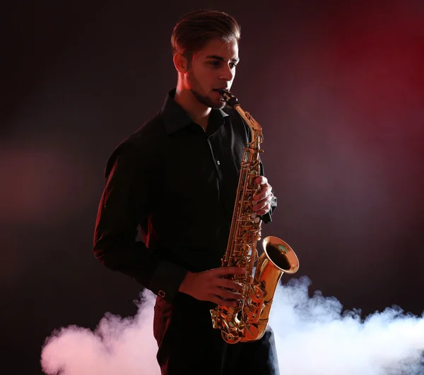 Jovem profissionalmente joga sax na fumaça vermelha — Fotografia de Stock