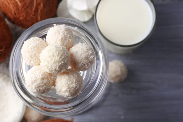 Candies in coconut flakes and fresh coconut on color wooden background