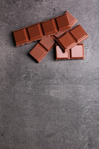 Mjölk choklad bitar på grå bakgrund — Stockfoto