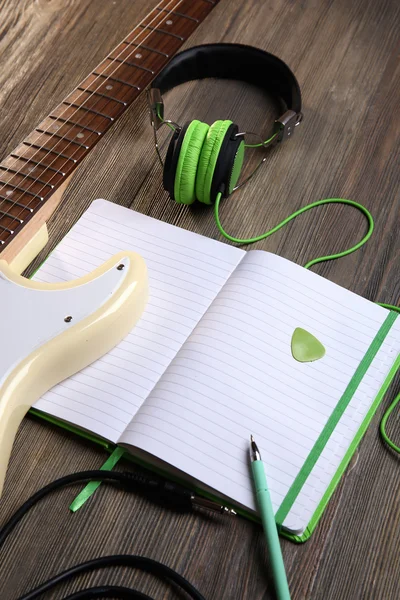 Electric guitar with green headphones and note book on wooden background — Stock Photo, Image