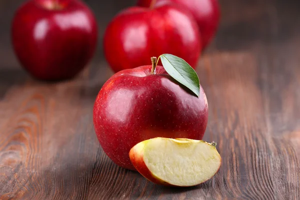Röda äpplen med löv och skiva på träbord, närbild — Stockfoto