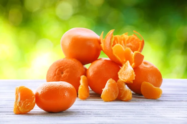 Reife Mandarinen auf Holztisch vor verschwommenem Naturhintergrund — Stockfoto