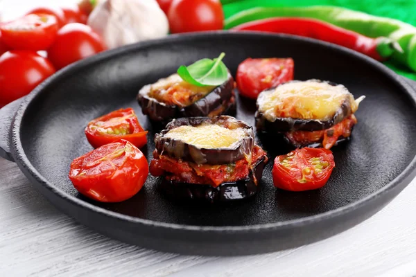 Prato de berinjela com tomates cereja e queijo em panela preta em mesa de madeira, close-up — Fotografia de Stock