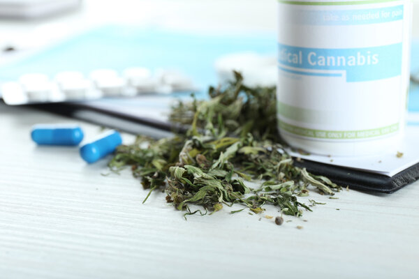 Бутылка сухой медицинской марихуаны и таблетки с планшетом на столе.
