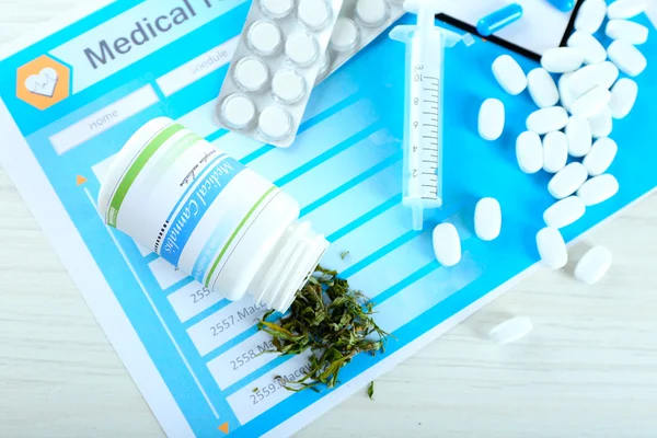 Bottle of dry medical cannabis and pills with clipboard on table close up — Stock Photo, Image