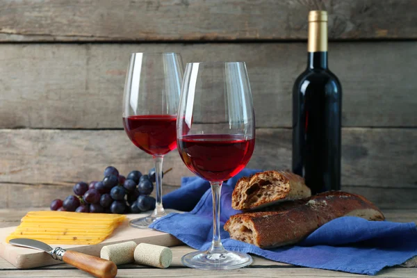 Still life of wine, grape, cheese and bread on rustic wooden background