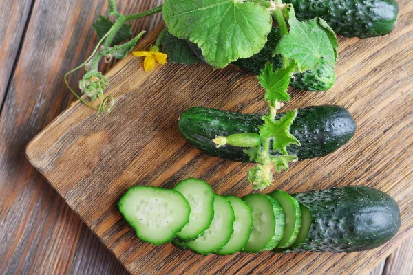 Gesneden komkommers en keuken bestuur op houten achtergrond — Stockfoto
