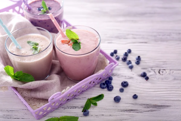 Savoureux yaourt aux fraises, bleuets et lait sur serveur sur fond de bois clair — Photo