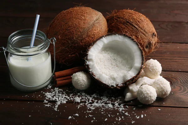 Candies in coconut flakes and fresh coconut on dark wooden background — Stock Photo, Image