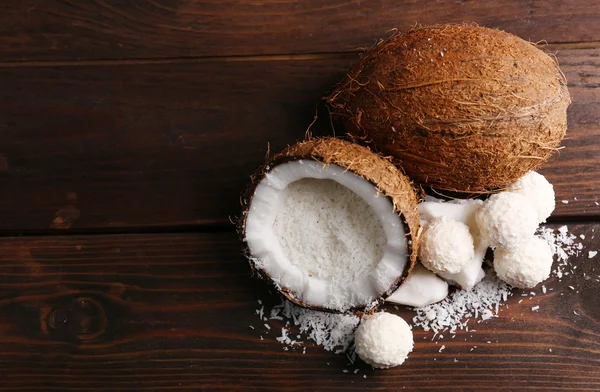 Godis i kokosflingor och färsk kokos på mörk trä bakgrund — Stockfoto
