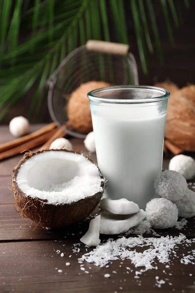 Caramelos en copos de coco, vaso de leche y coco fresco sobre fondo de madera oscura —  Fotos de Stock