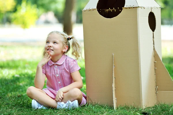 Liten flicka sitter nära carton raket — Stockfoto