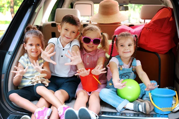 Tres hermosas chicas y un niño se sientan en el maletero de un coche y se ríen —  Fotos de Stock