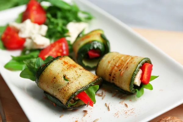 Zucchini rolls with cheese, bell peppers and arugula on plate, close-up, on table background — Stock Photo, Image