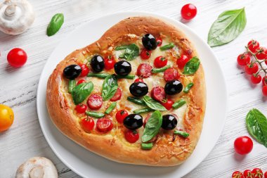 Sebze ve otlar ahşap arka plan üzerinde taze lezzetli kalp pizza şeklinde süslenmiş