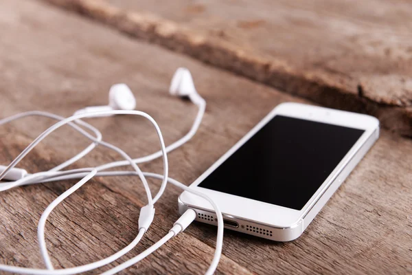 Celular branco com fones de ouvido em fundo de madeira — Fotografia de Stock