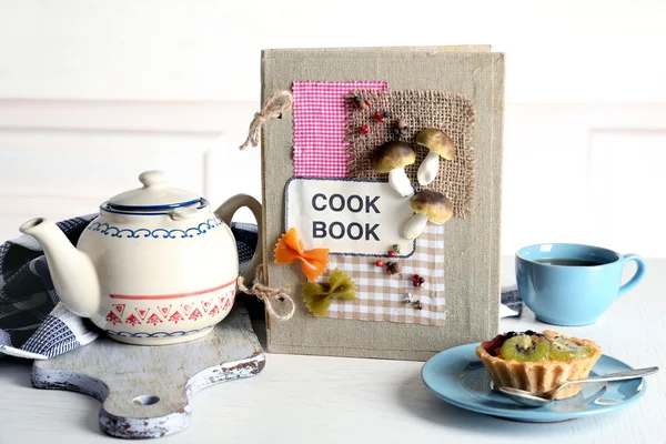 Libro di cucina decorato con teiera e gustosa torta — Foto Stock