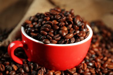 Kırmızı bir fincan ve aromatik kahve çekirdekleri arka plan çuval bezi üzerinde dağınık