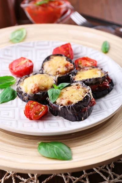 Dish of eggplant with cherry tomatoes and cheese in white plate on wooden table, closeup — Stock Photo, Image