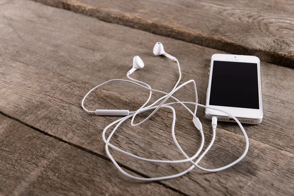 Celular branco com fones de ouvido em fundo de madeira — Fotografia de Stock