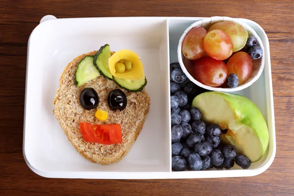 Caja de almuerzo con sándwich creativo y frutas sobre fondo de madera — Foto de Stock