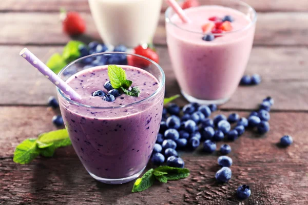Chutné borůvek, jahod a mléčné jogurty s bobule a mátou kolem na dřevěné pozadí — Stock fotografie