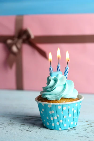 Pembe mevcut kutuları karşı mavi ahşap masa mum ile tatlı kek — Stok fotoğraf