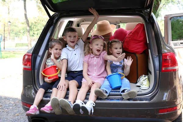 Trois belles filles et un garçon assis sur un coffre de voiture et riant — Photo