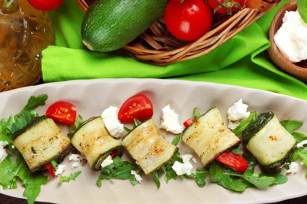 Zucchini rolls with cheese, bell peppers and arugula on plate, close-up, on table background — Stock Photo, Image