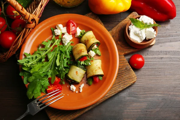 Zucchini rolls with cheese, bell peppers and arugula on plate, close-up, on table background — Stock Photo, Image