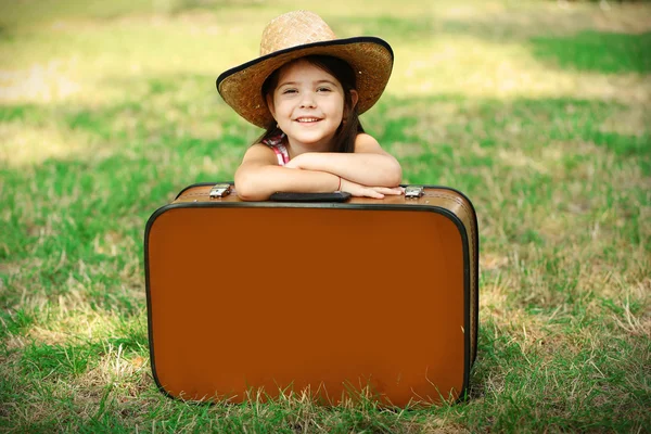 Szczęśliwa dziewczynka w kapeluszu siedzi za walizkę — Zdjęcie stockowe
