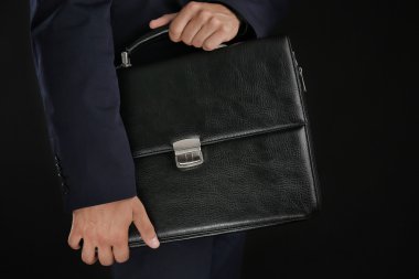 Koyu arka plan üzerinde evrak çantası ile takım elbiseli şık adam